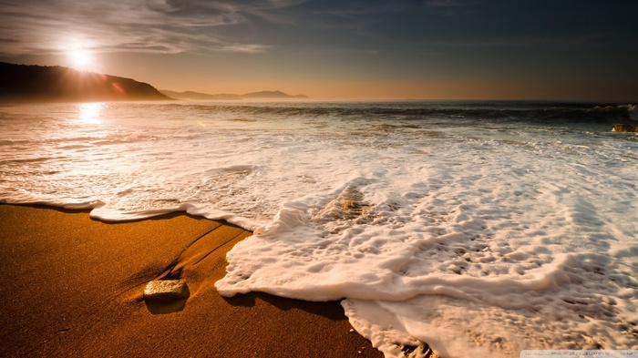 Sunrise over a sandy beach with waves and a cliff