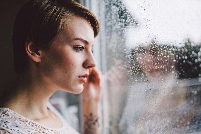 Woman with short hair looking out a rainy window