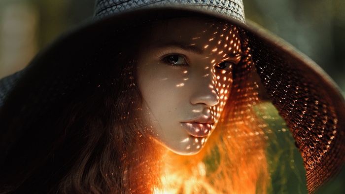 Woman in a wide-brimmed hat with dappled sunlight on her face
