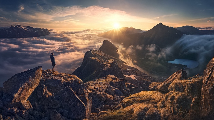 Man standing on mountain peak above clouds at sunset