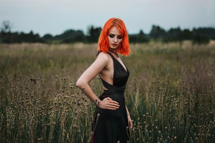 Woman with orange hair in a black dress in a field