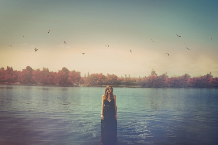 Woman in a black dress standing in water with birds flying