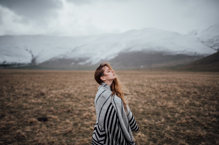 Woman wrapped in a blanket in a field with mountains
