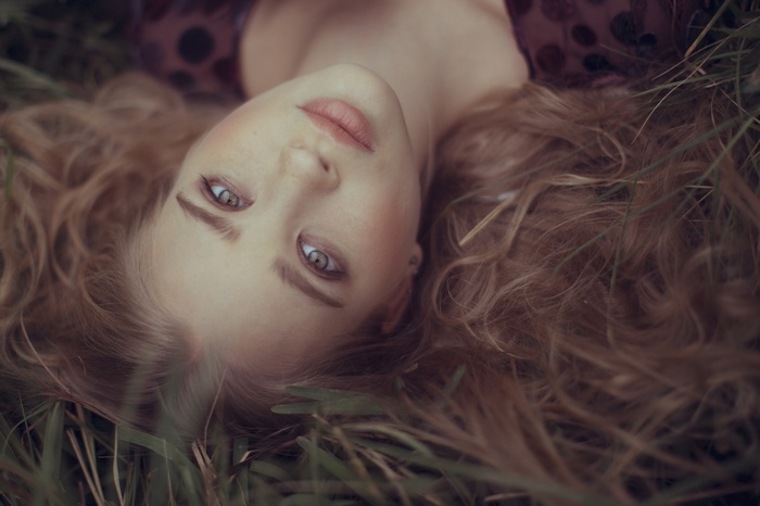 Woman with curly hair lying upside down in grass