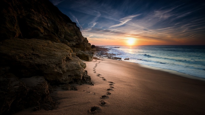 Footprints on a sandy beach at sunset with a cliff