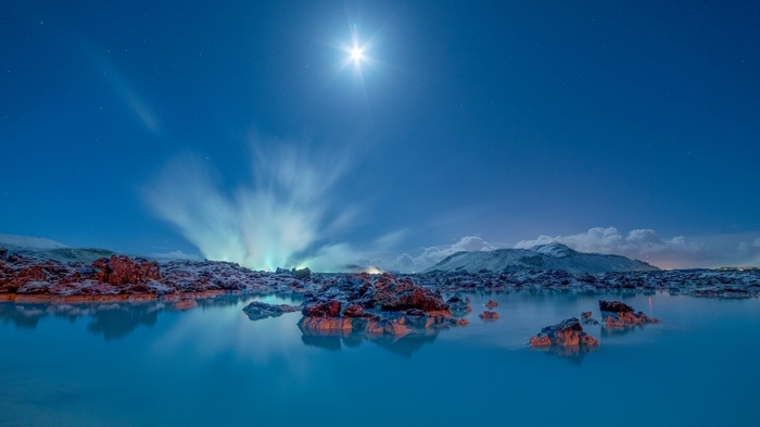 Moonlit night over Iceland's snowy landscape and lagoon