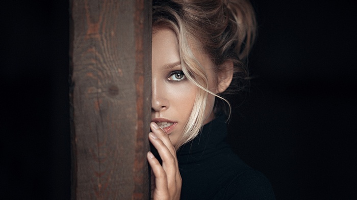 Portrait of a blonde woman peeking from behind a wooden beam