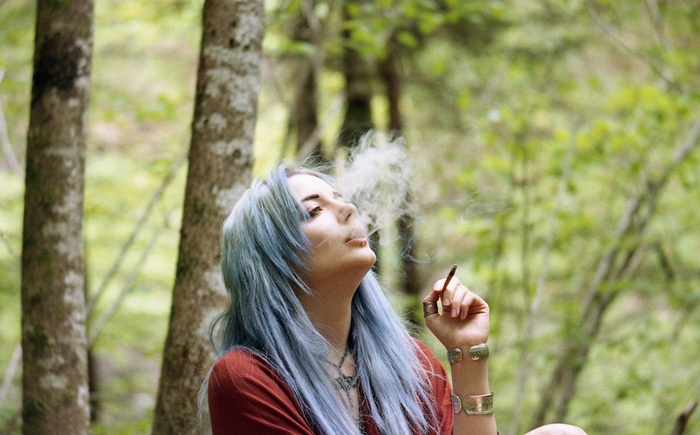 Woman with blue hair smoking in a forest