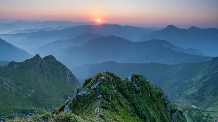 Misty mountain range at sunset with sun low on horizon