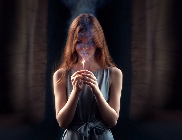 Woman holding a lit match with smoke