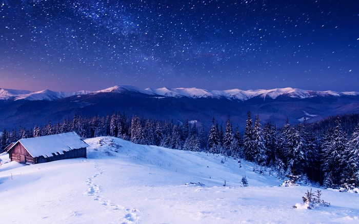 Winter night sky over snow-covered mountains and cabin