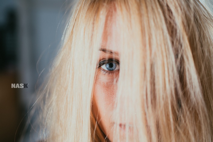 Woman with blonde hair covering her face, blue eye visible
