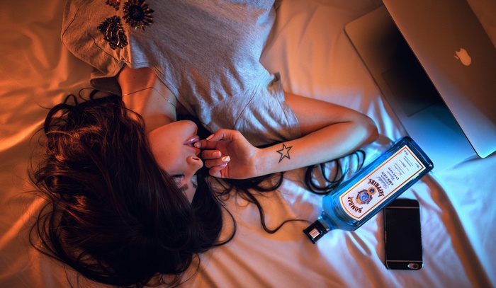 Woman lying on bed with MacBook, iPhone, and Bombay Sapphire