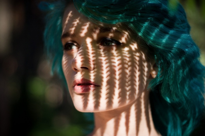 Woman with teal hair and leaf shadows on face