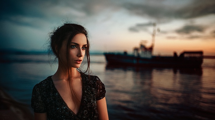 Woman in dress by the water with a ship at sunset