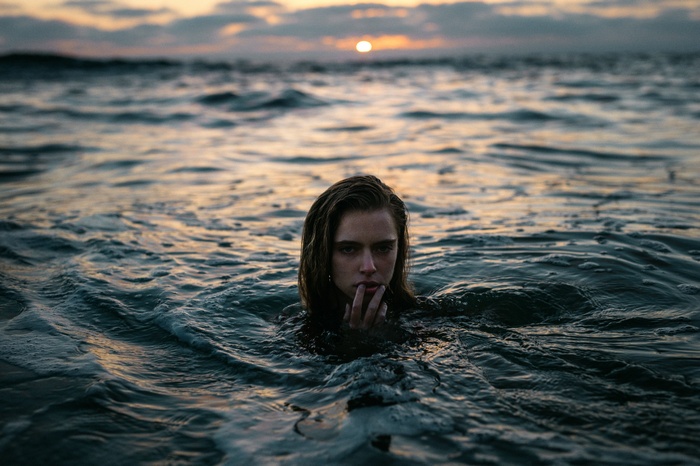 Woman emerging from ocean waves at sunset