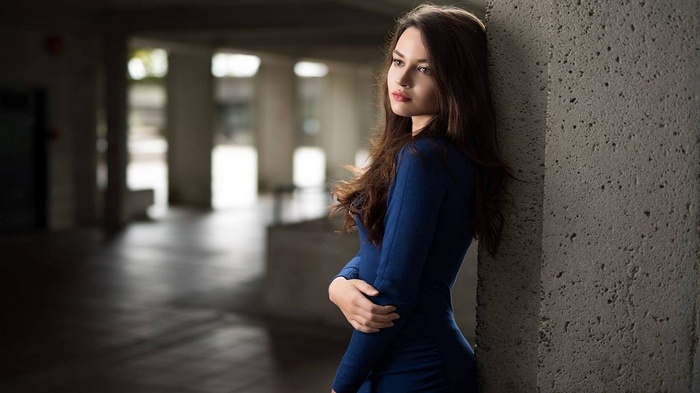 Woman in blue dress leaning against concrete pillar