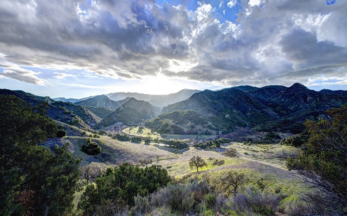 Sunlight over a mountain valley with trees and clouds