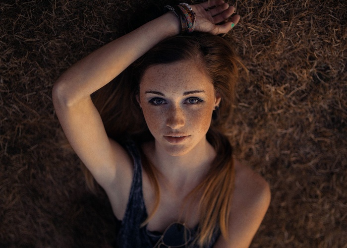 Woman with freckles lying down on dry grass