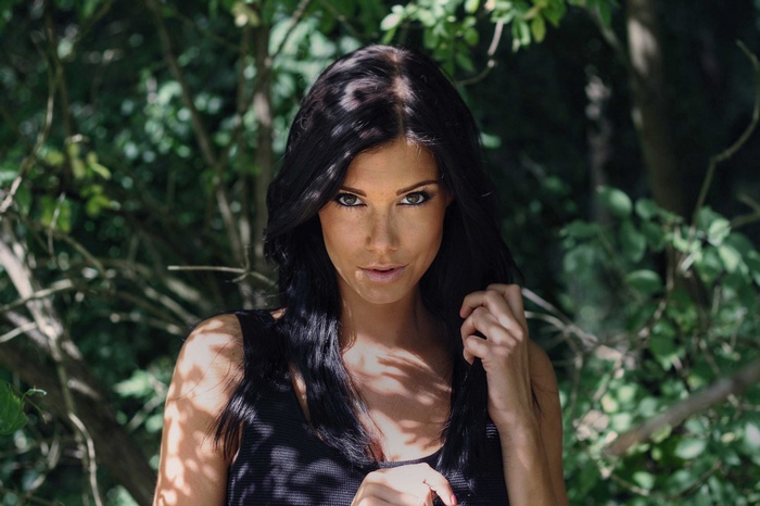 Woman with black hair and freckles in dappled sunlight