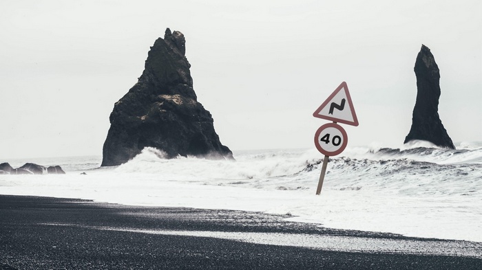 Road signs on a black sand beach with waves and rock formations