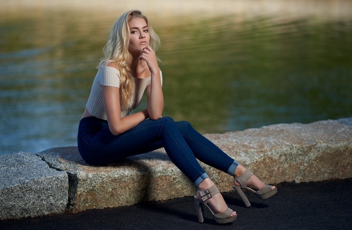Woman in jeans and high heels sitting by water