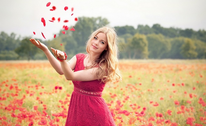 Woman in red dress throwing petals in a poppy field