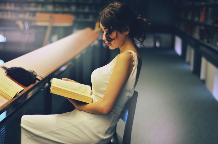 Woman in white dress reading a book in a library