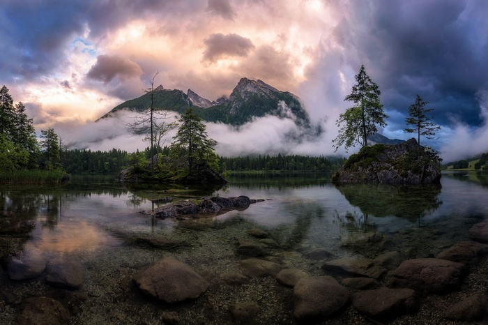 Lake with mountains and trees under dramatic clouds