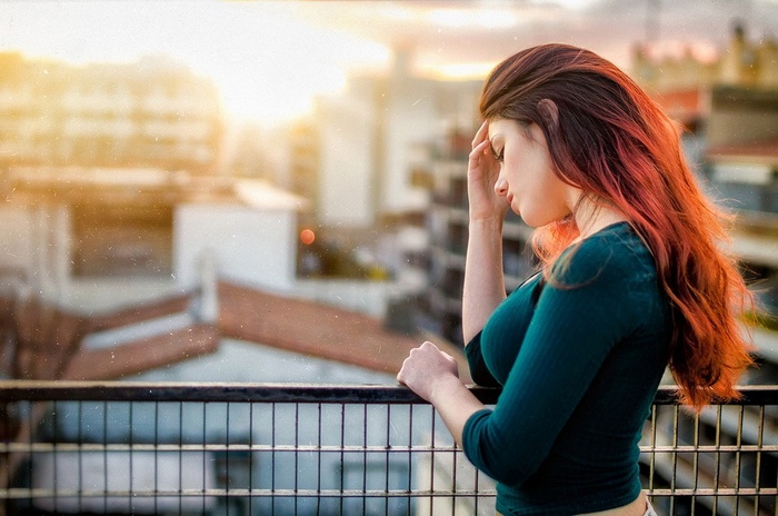 Redhead woman with hand on forehead on a balcony
