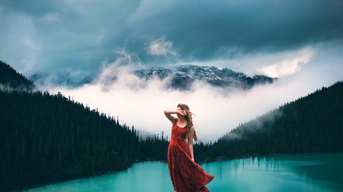 Woman in red dress by a turquoise lake with mountains