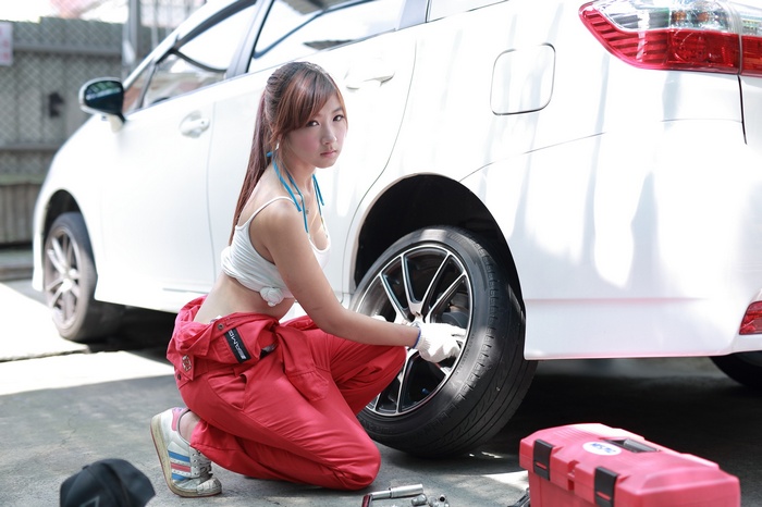 Asian woman in red overalls fixing a car tire