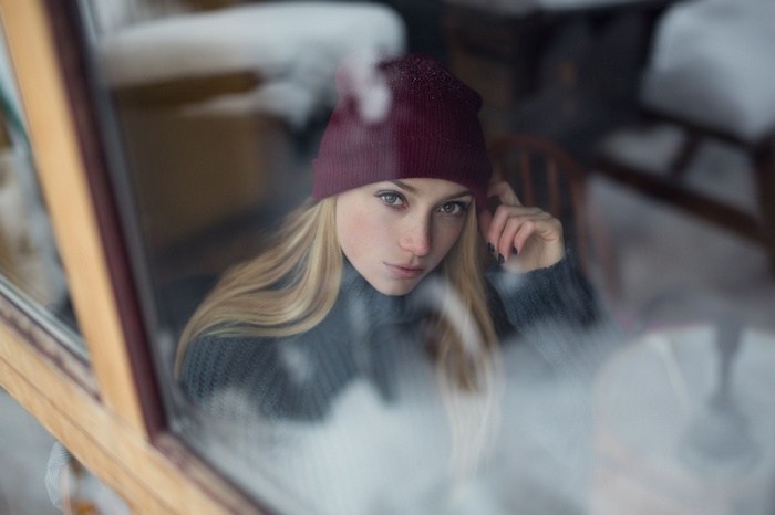 Woman in beanie and sweater looking through window