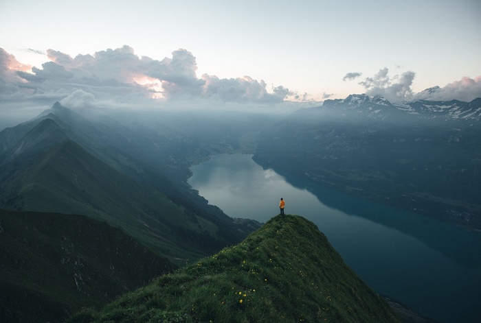 Man on mountain peak overlooking lake and mountains