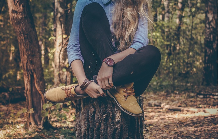 Woman with blonde hair sitting on a tree stump in a forest