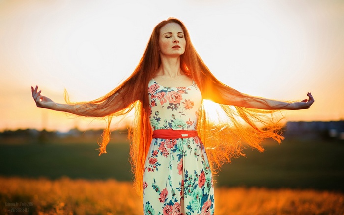 Redhead woman with long hair in a floral dress at sunset