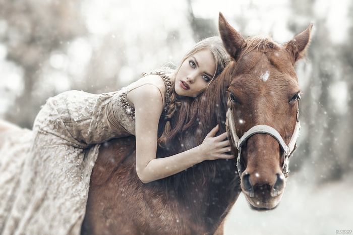 Woman in a dress lying on a horse in snow
