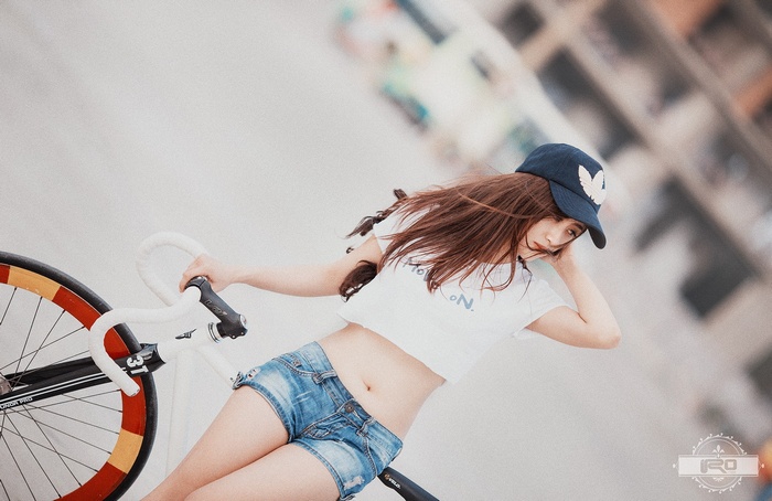 Asian woman with bicycle wearing denim shorts and baseball cap