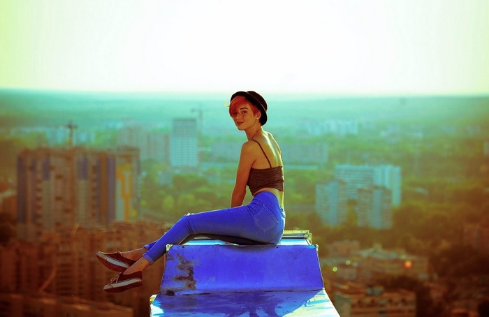 Redhead woman with short hair wearing a hat and jeans on a rooftop