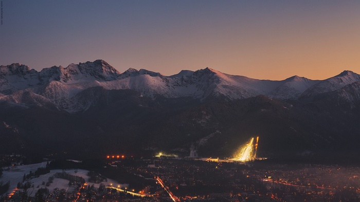 Zakopane ski jump illuminated at dusk with snowy mountains