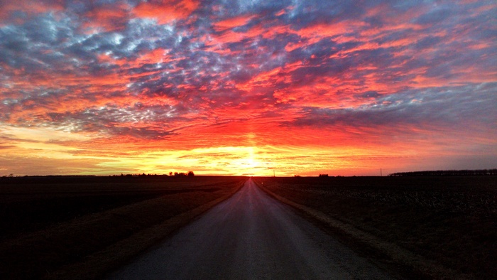 Road through fields at sunset with colorful clouds