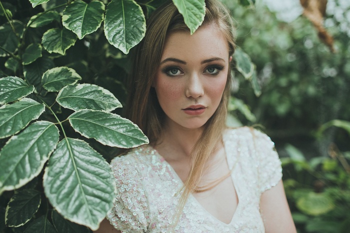 Woman with blonde hair in a sequined dress surrounded by leaves