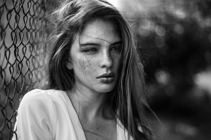 Monochrome portrait of a woman with freckles near a fence