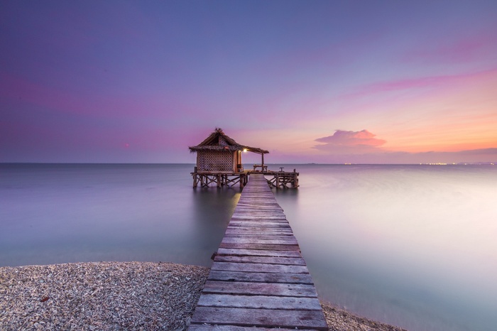 Wooden pier leading to a hut over the sea at sunset