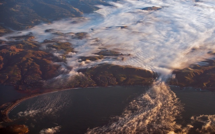 Aerial view of a misty coastline with rolling hills