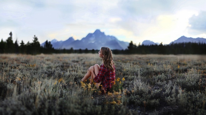 Woman sitting in a field with mountains in the background