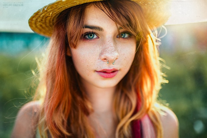 Woman with red hair wearing a straw hat and septum piercing
