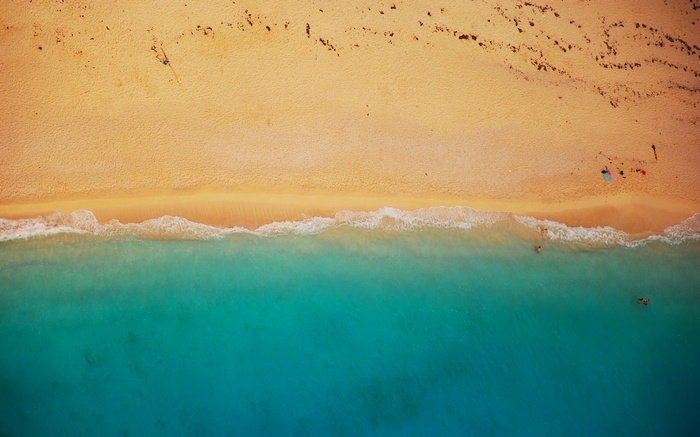 Aerial view of a sandy beach with turquoise water and people swimming