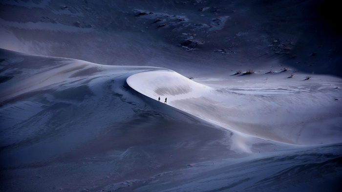Two people walk on a sand dune in the desert