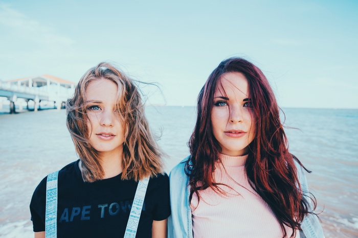 Two women on a beach with a pier